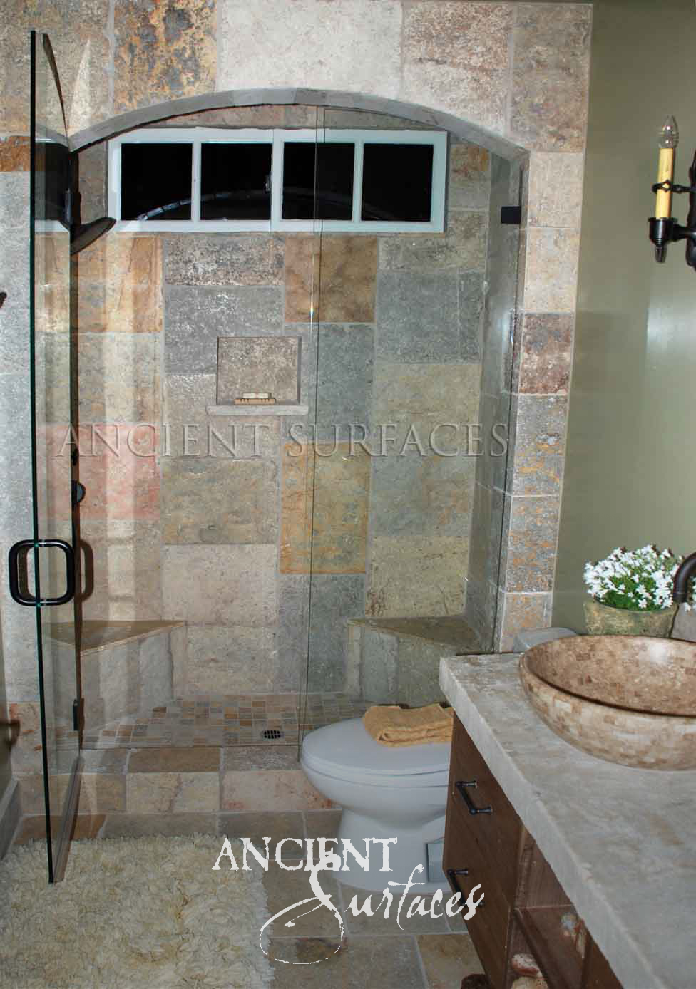 Ancient Surfaces Biblos Limestone tiles in grey, gold and rust tones lining an arched shower enclosure and bathroom floor