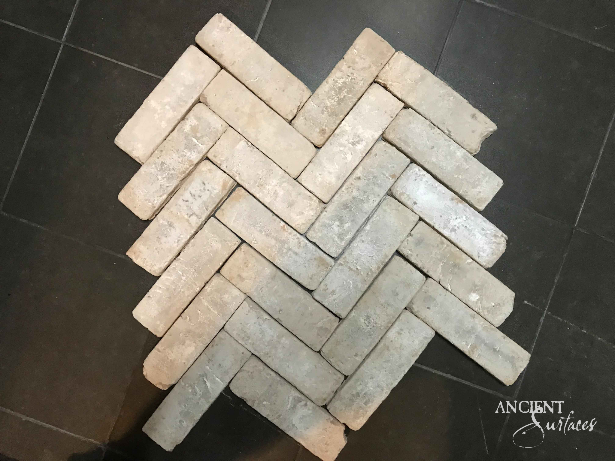 Reclaimed antique brick pavers from Ancient Surfaces laid dry in a herringbone panel on a dark stone floor