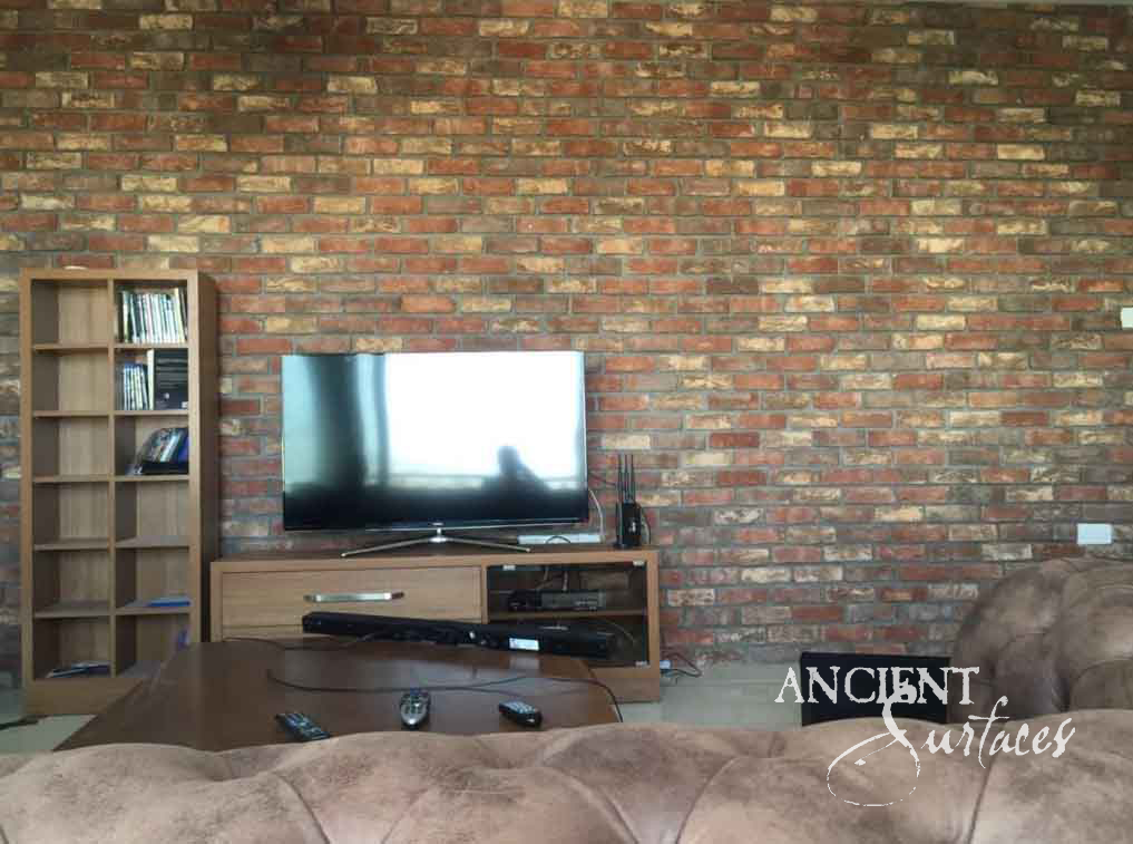 Reclaimed antique brick feature wall from Ancient Surfaces in red and umber tones behind a living room media console